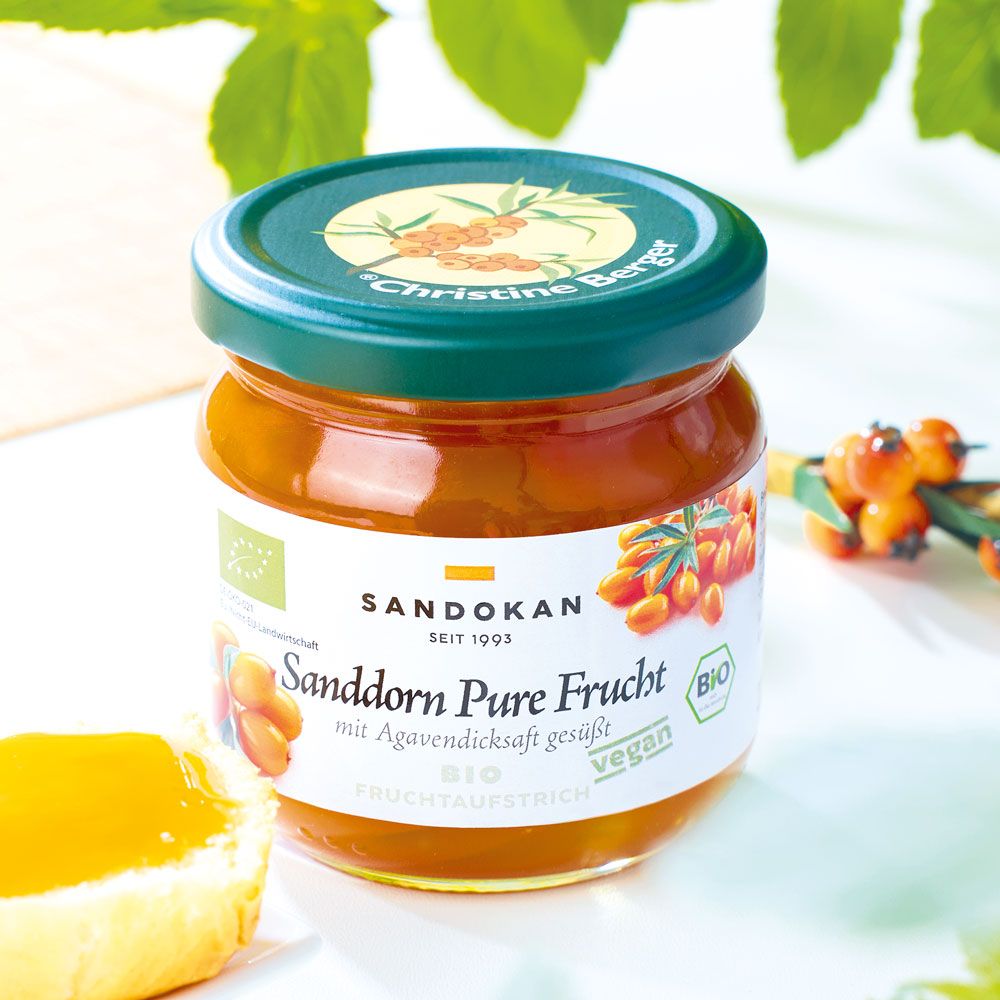 Glas Sanddorn-Fruchtaufstrich. Etikett mit Text und Bio-Siegel. Grüner Deckel. Vegan. Auf Tisch.