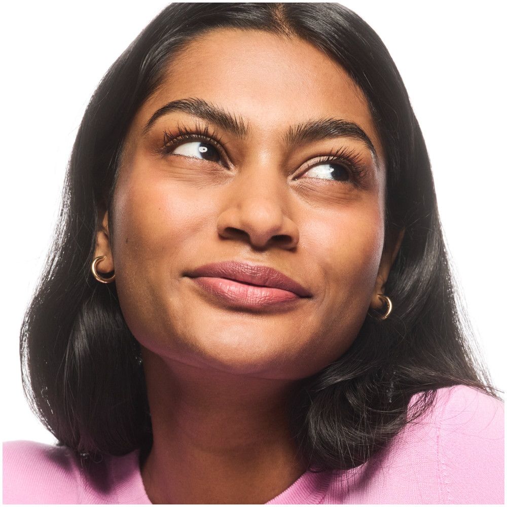 Porträt einer Frau mit dunklen Haaren, die nach oben blickt. Sie trägt einen rosafarbenen Pullover und goldene Ohrringe.