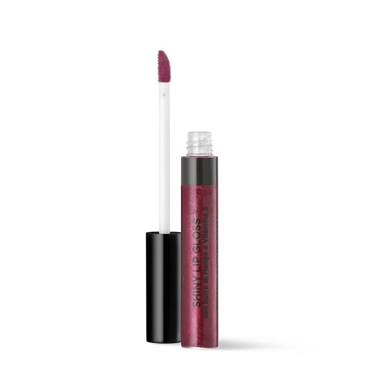 Bottega Verde Shiny Lip Gloss. Un tubetto di lucidalabbra trasparente e scintillante con tappo nero e applicatore bianco. L'applicatore è ricoperto di prodotto lucidalabbra bordeaux. Sul tubetto è scritto "Shiny Lip Gloss" e "con vitamina E".