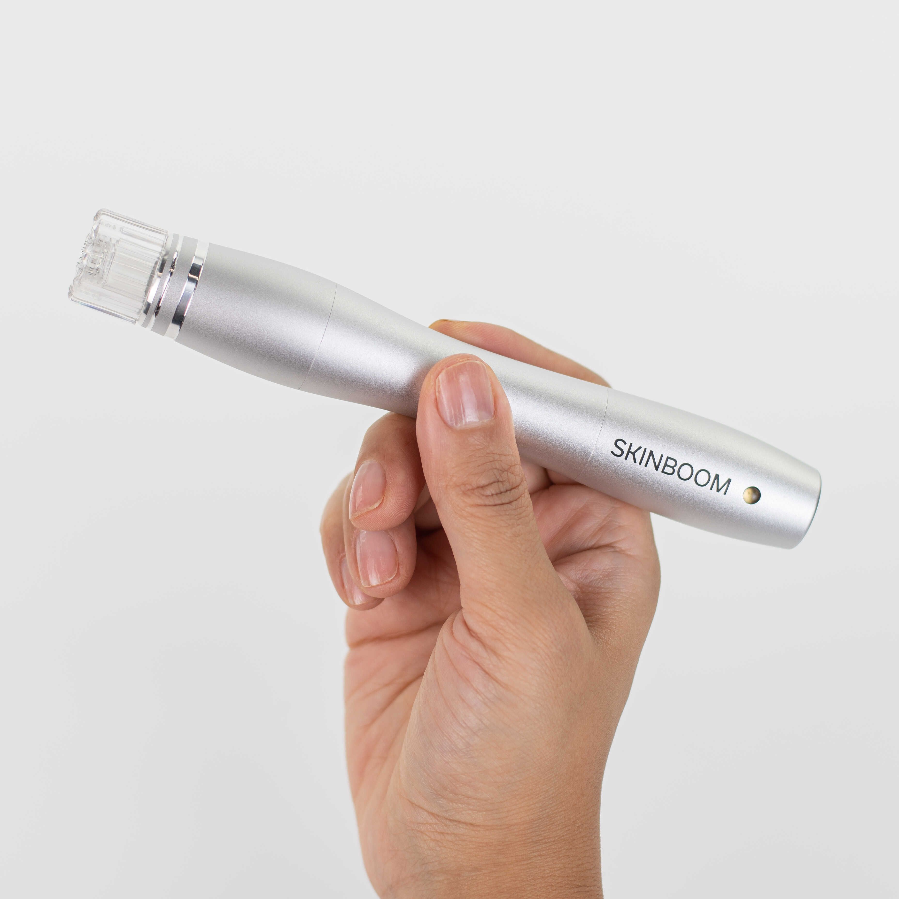Silberfarbenes SKINBOOM-Gerät in einer Hand gehalten. Der Stift hat eine zylindrische Form mit dem Markennamen.