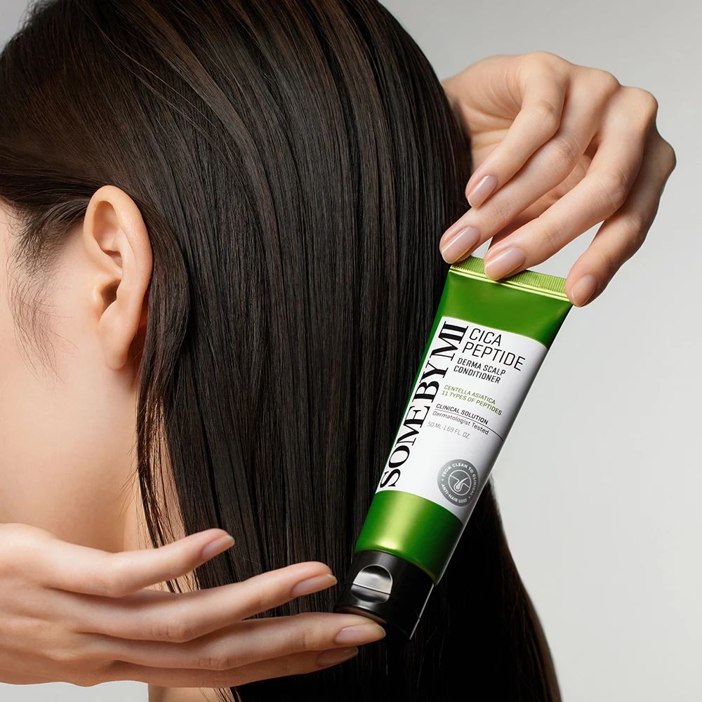 Grüne Tube mit schwarzem Deckel. Aufschrift SOME BY MI Cica Peptide Derma Scalp Conditioner. Hände halten die Tube neben dunklem Haar.