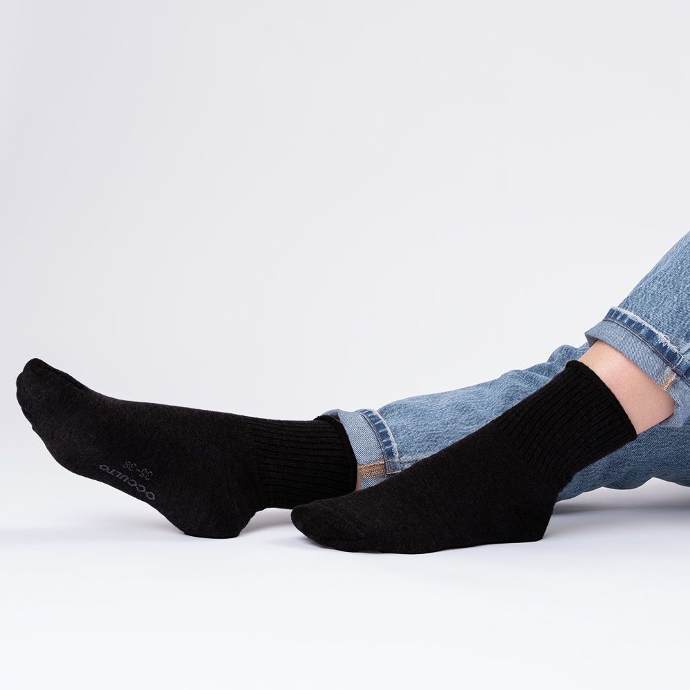 Schwarze Socken ohne Gummibund, von der Seite auf einer sitzenden Person.