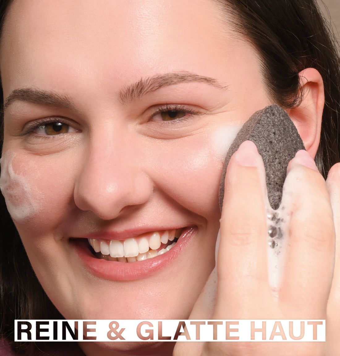 Frau verwendet einen Konjac-Schwamm auf ihrem Gesicht. Schaum. Text: Reine & glatte Haut.