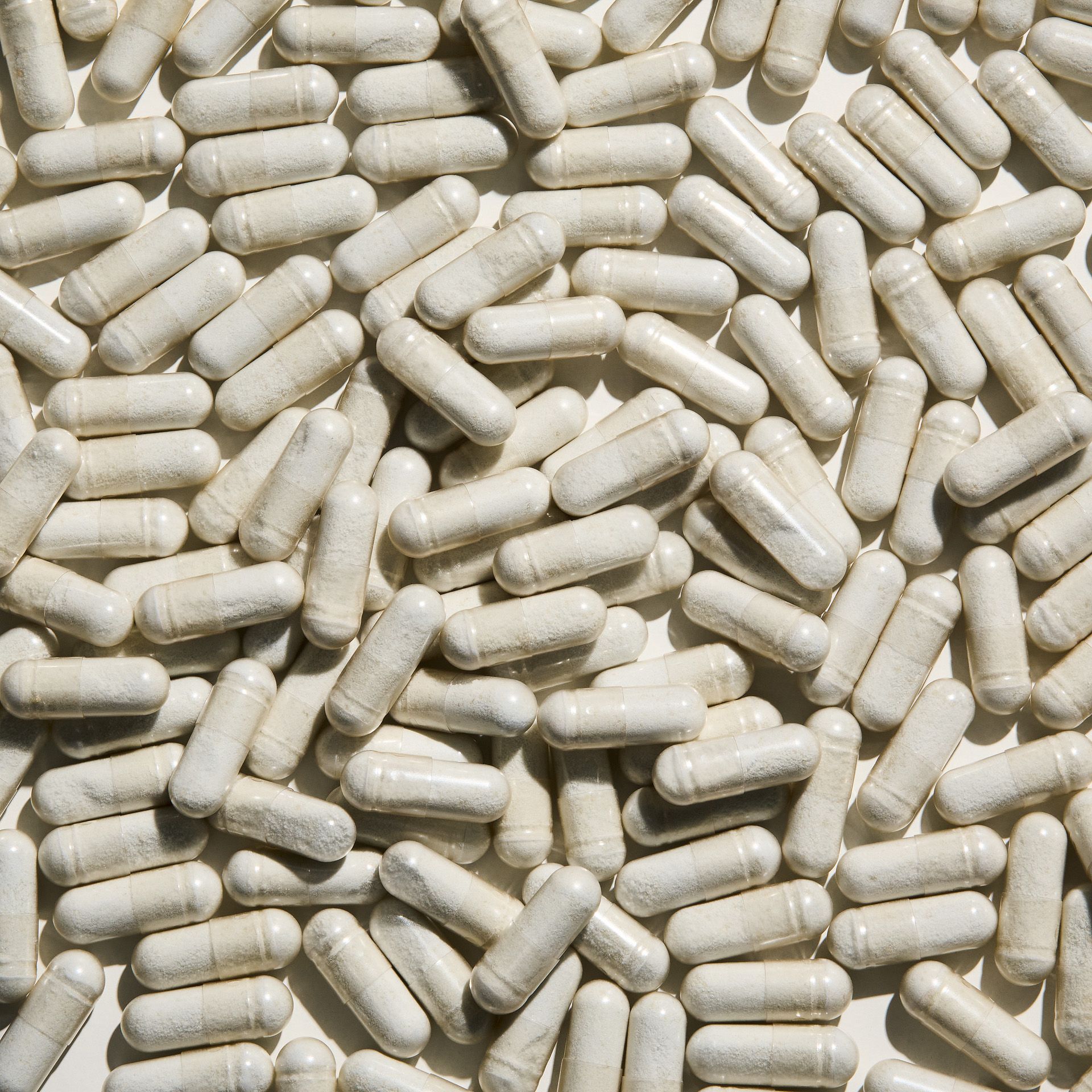 Viele weiße Kapseln, länglich, auf weißem Hintergrund. Keine Verpackung sichtbar.