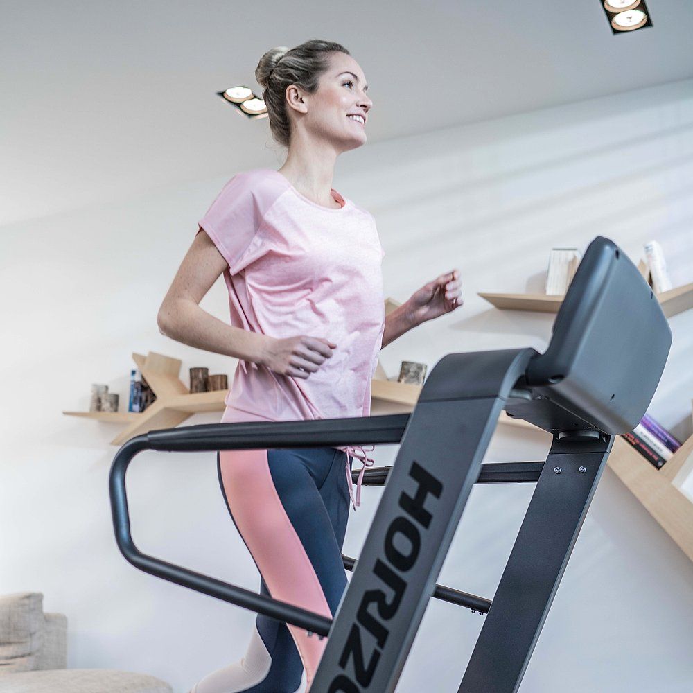 Frau läuft auf einem Laufband. Laufband mit Horizon-Logo. Frau trägt Sportkleidung.