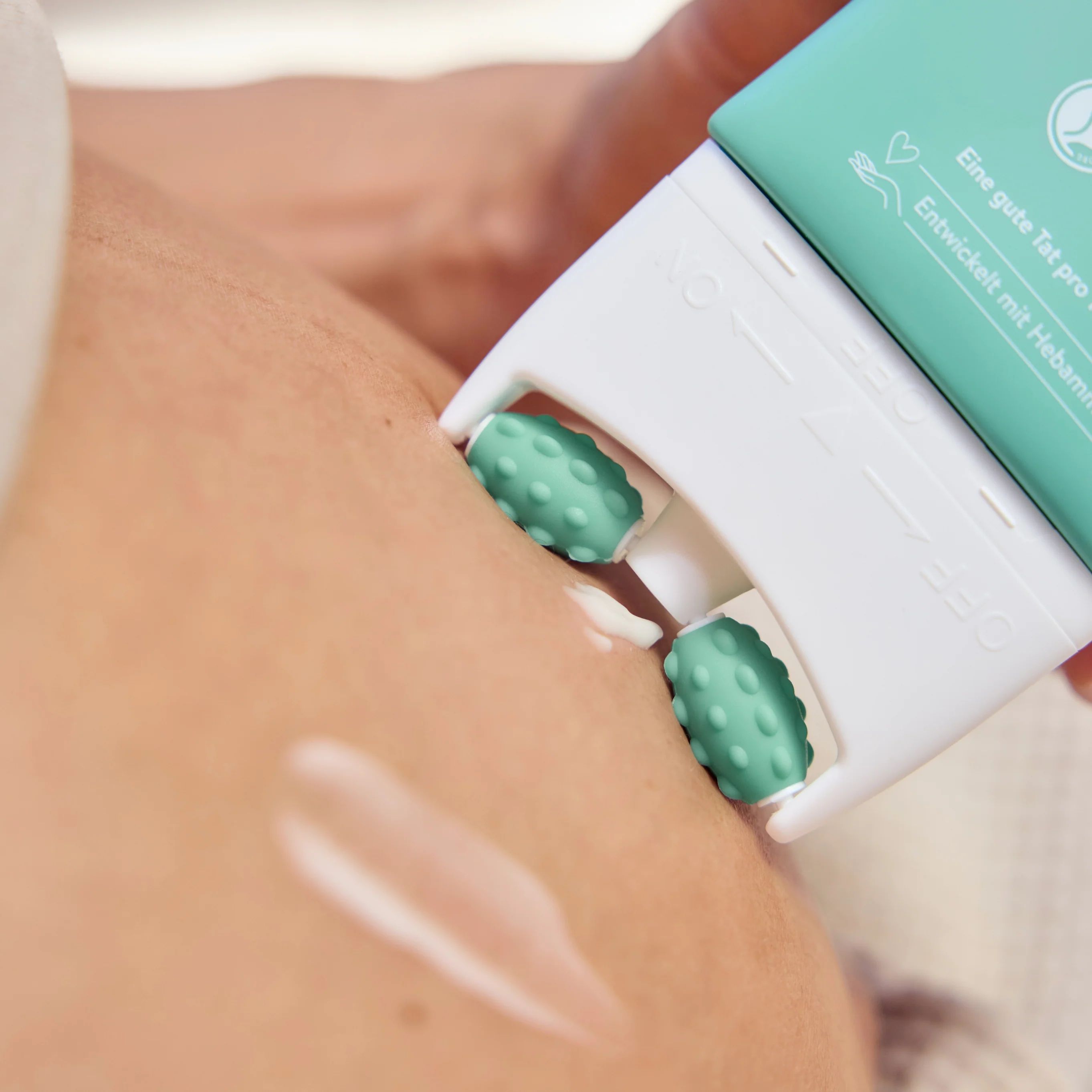 Nahaufnahme des Massageaufsatzes der MABYEN Pflegelotion Mama. Zwei grüne Rollen massieren die Haut. Creme ist sichtbar.