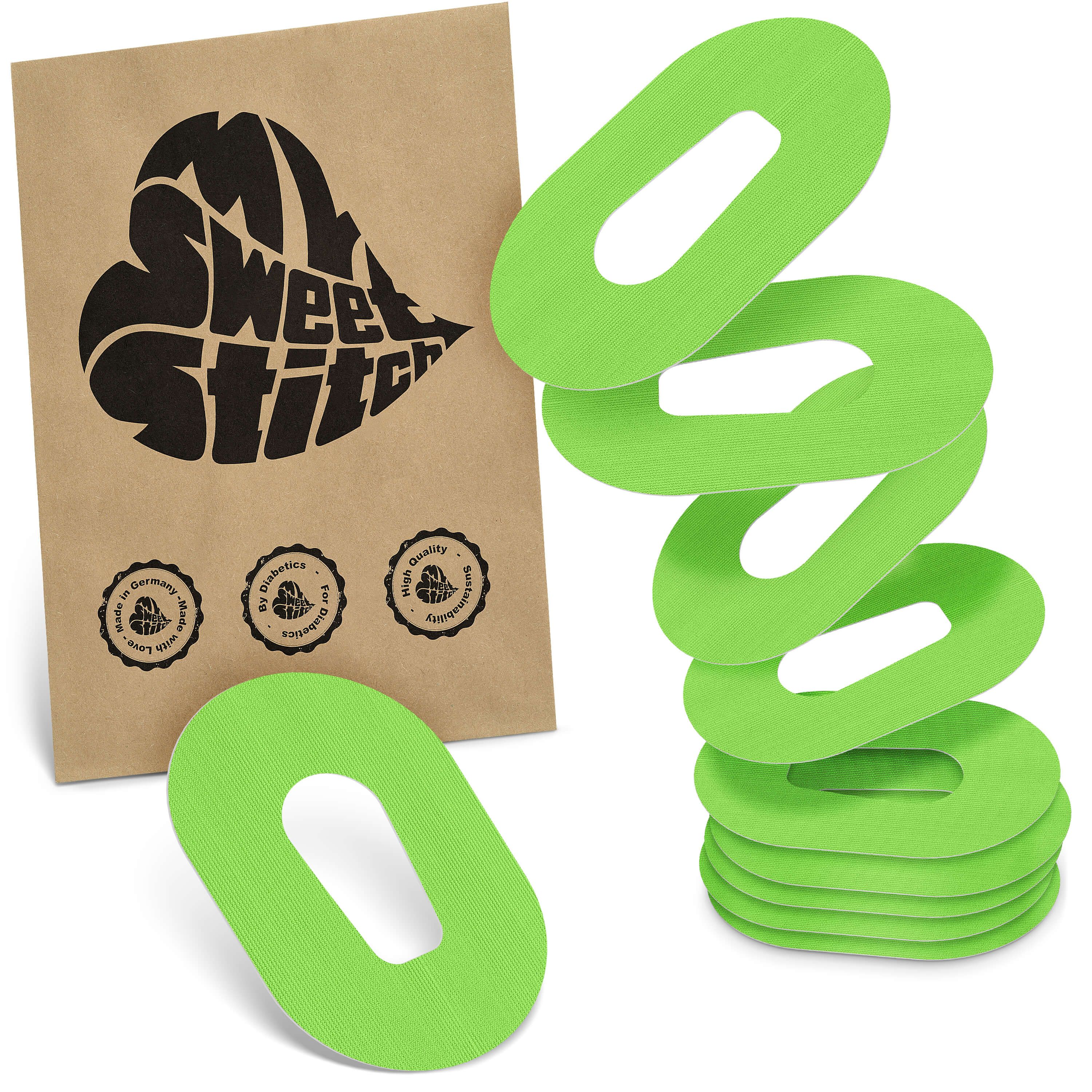 Fixierpflaster, grün, oval mit Aussparung. Braune Verpackung mit Logo und Siegeln.