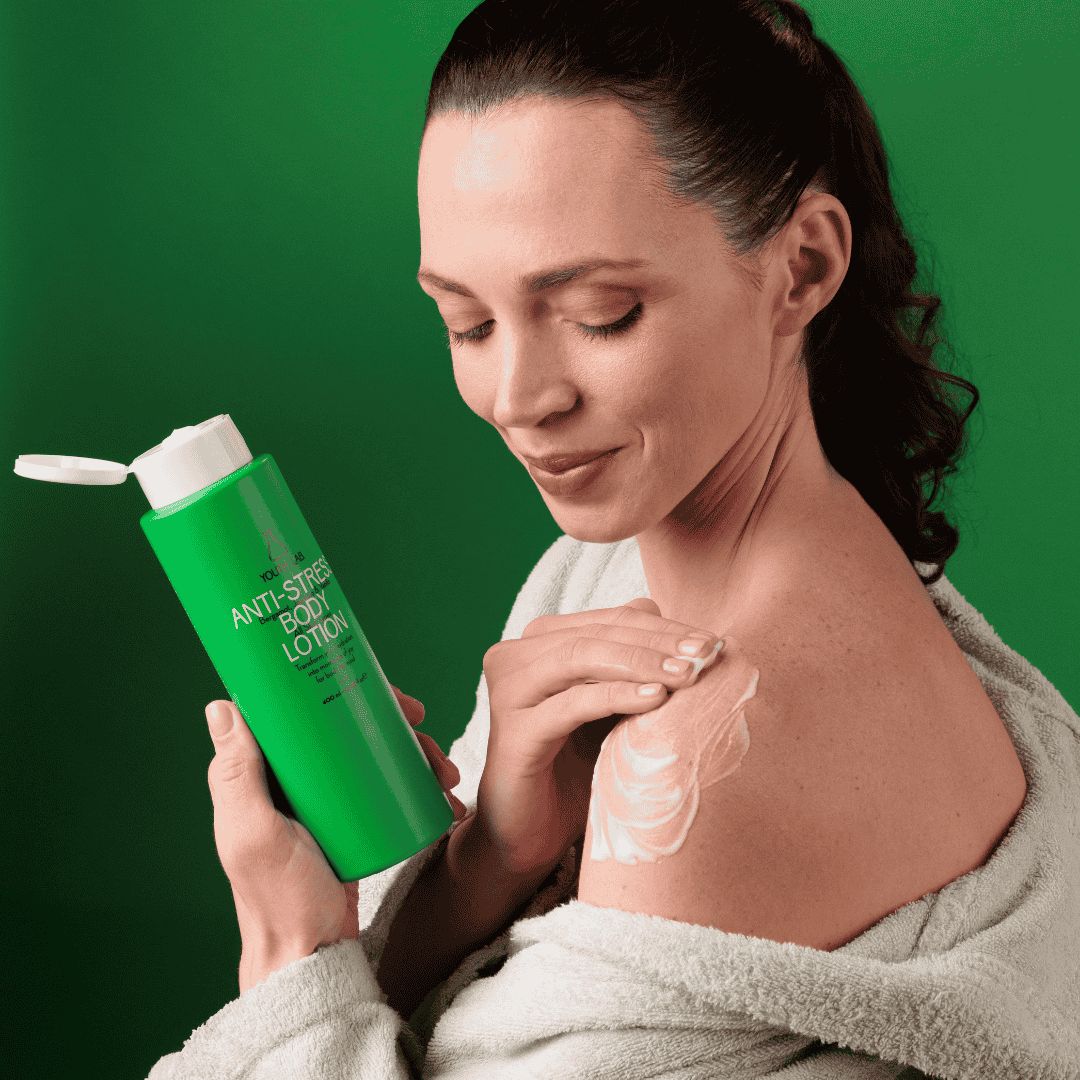 Frau trägt Lotion auf Schulter auf. Grüne Flasche mit weißem Deckel. Aufschrift: Anti-Stress Body Lotion.