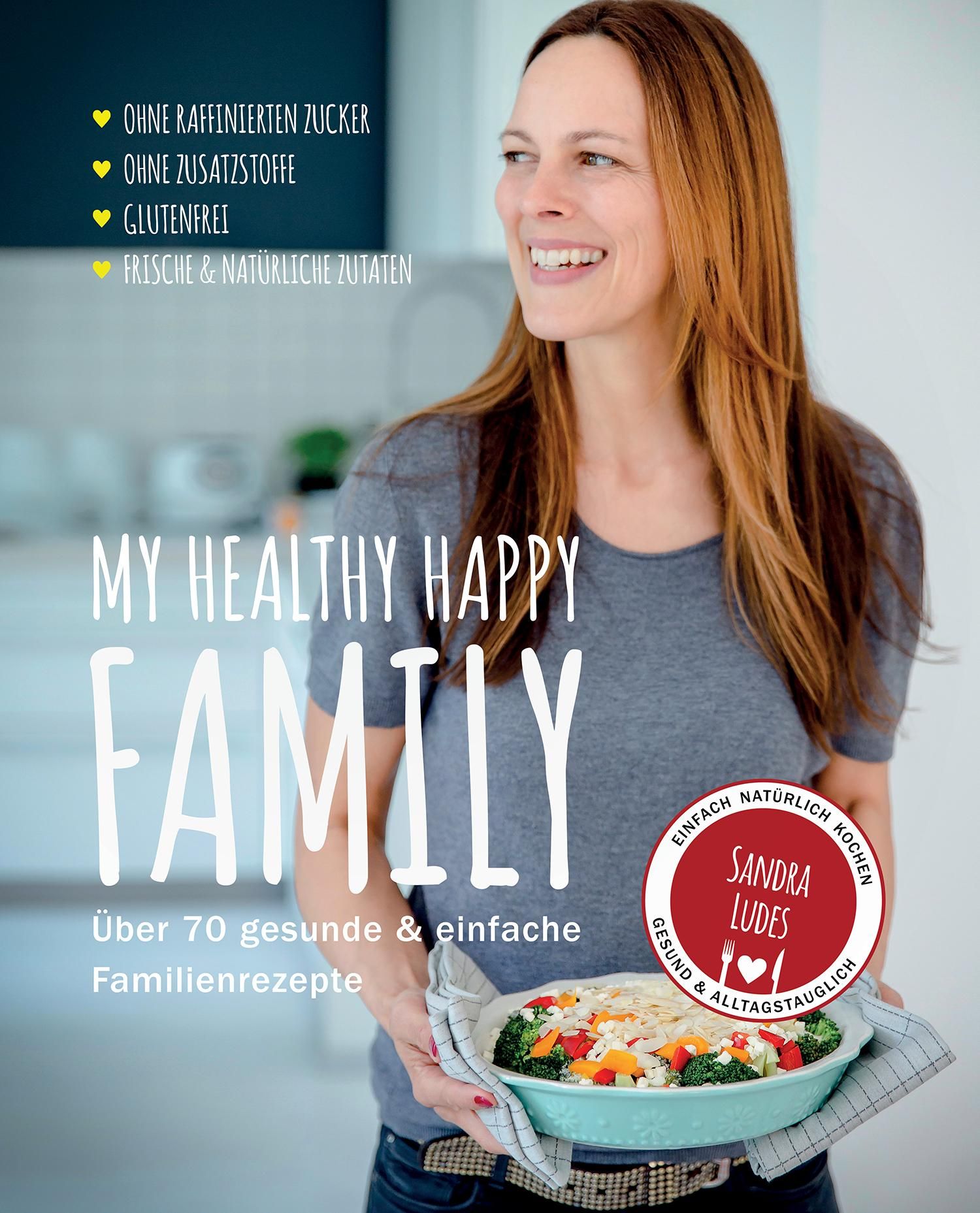 Buchcover: "My Healthy Happy Family". Frau hält Auflaufform mit Gemüse. Text: Ohne raffinierten Zucker, ohne Zusatzstoffe, glutenfrei, frische & natürliche Zutaten.