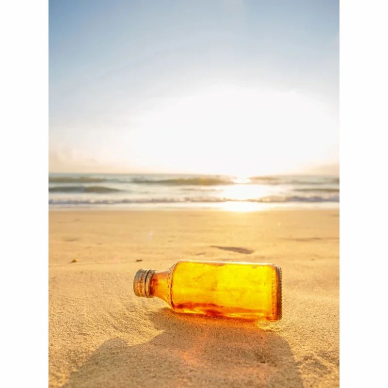 Gelbe Flasche am Strand im Sonnenlicht. Flasche liegt im Sand. Hintergrund: Meer und Sonne.