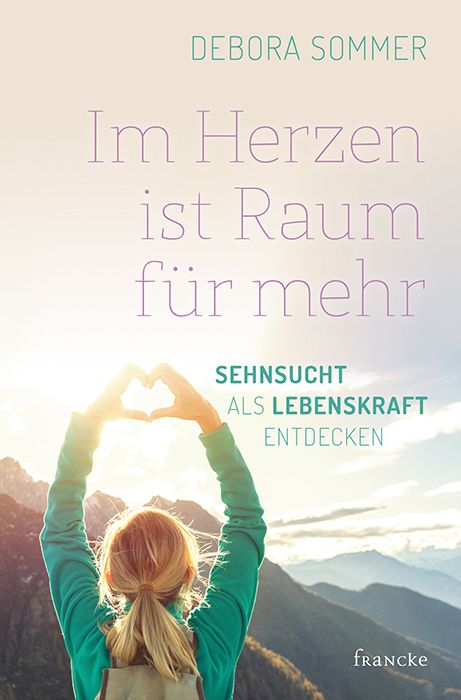 Buchcover. Titel: Im Herzen ist Raum für mehr. Autorin: Debora Sommer. Verlag: Francke. Frau formt Herz mit Händen vor Bergpanorama.