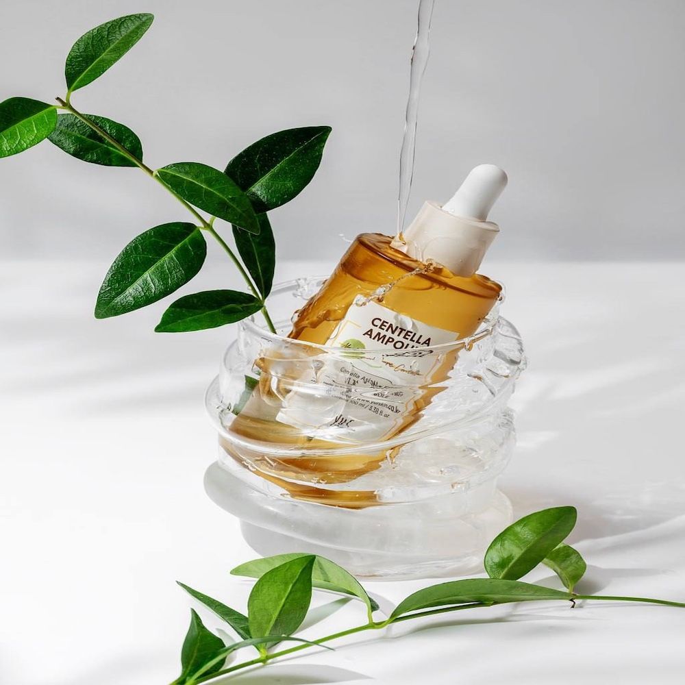 Serumflasche in Glasbehälter mit Wasser und Blättern. Aufschrift: Centella Ampoule.
