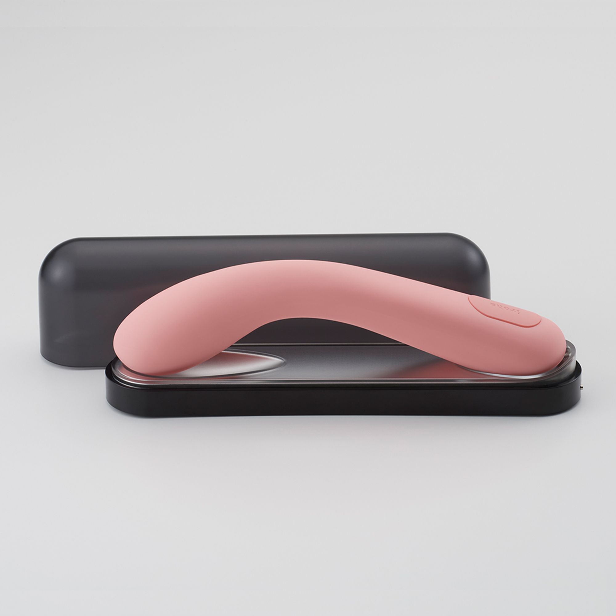 Rosa Vibrator auf schwarzer Basis, neben schwarzer Hülle. Produktname nicht sichtbar.