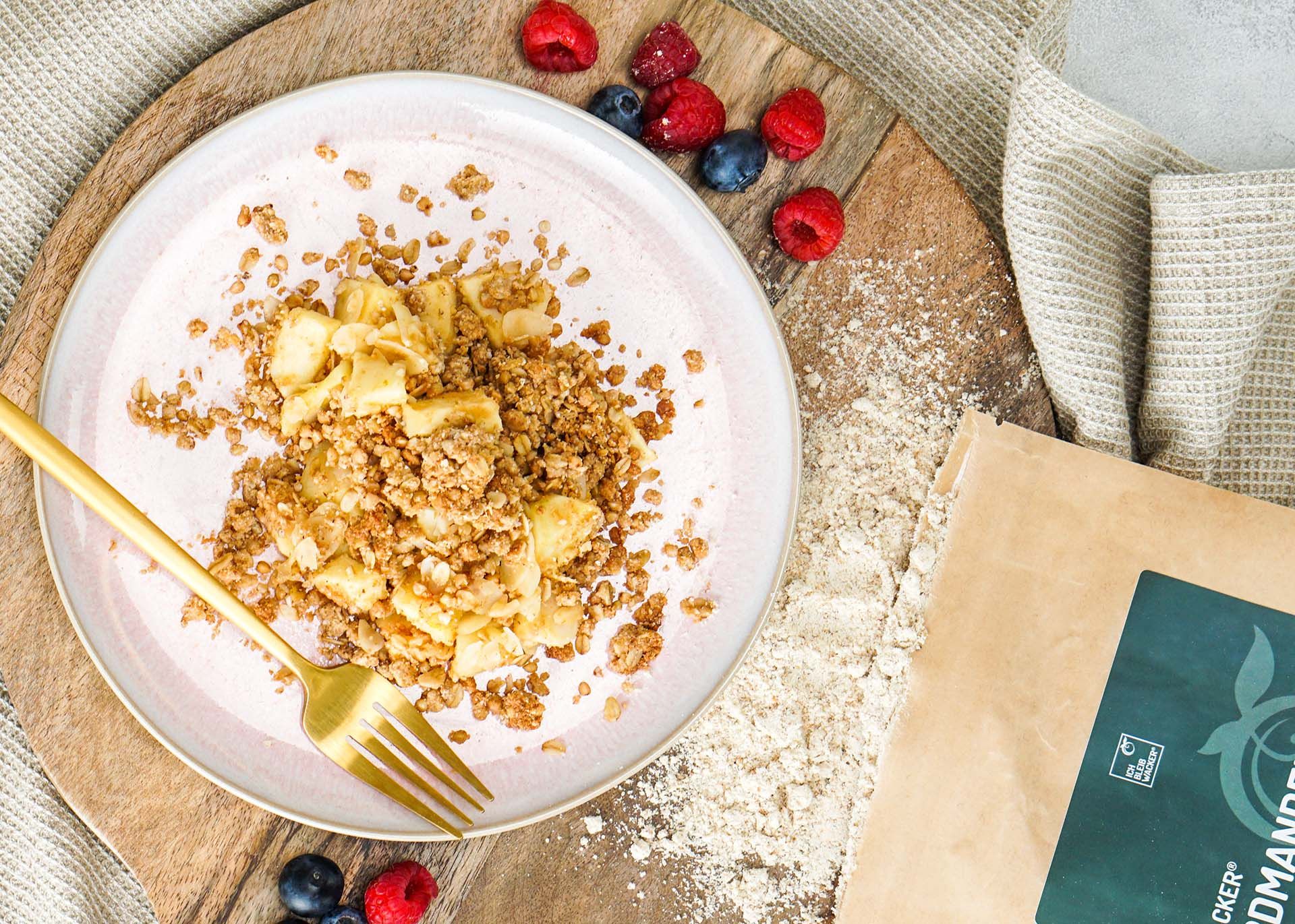 Teller mit Apfelstücken und Erdmandelflocken-Crumble. Daneben eine Tüte mit Erdmandelflocken und Beeren.