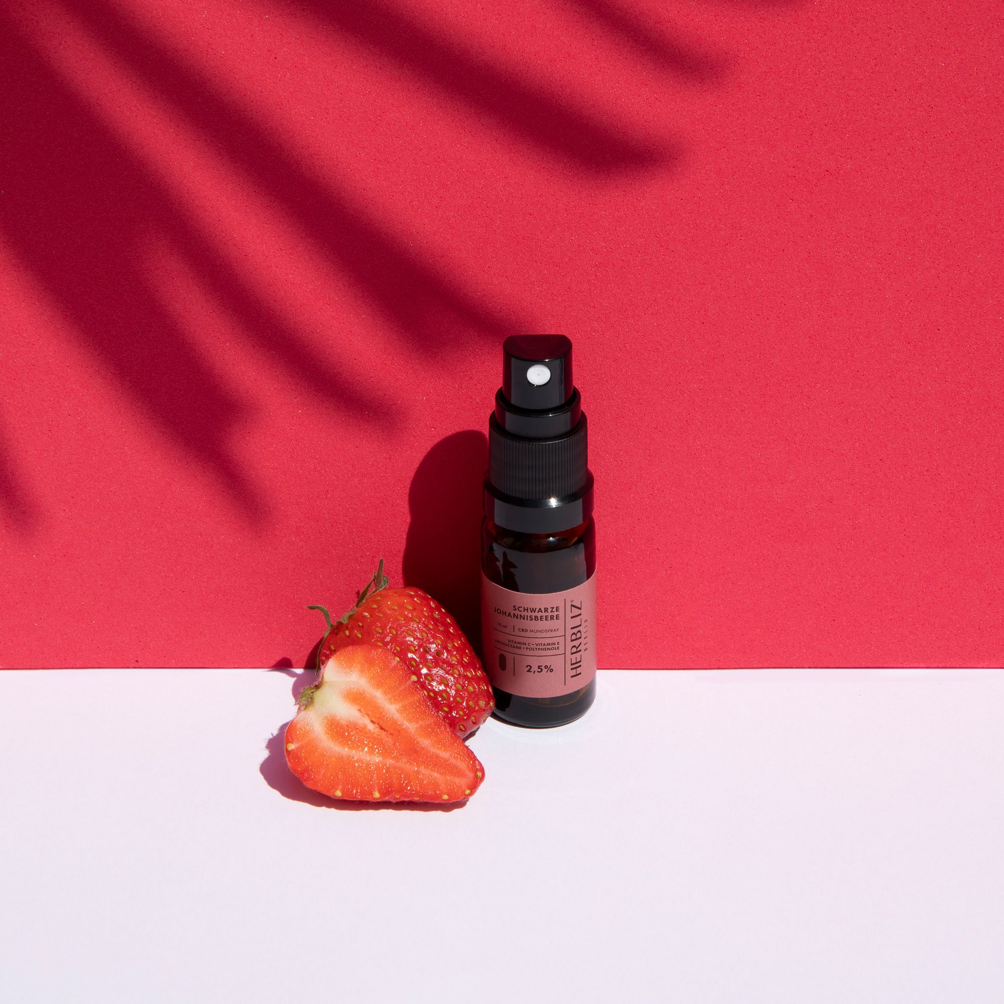 HERBLIZ Erdbeere CBD Öl, Flasche mit Erdbeeren. Flasche mit Sprühkopf, daneben zwei Erdbeeren auf rotem Hintergrund.