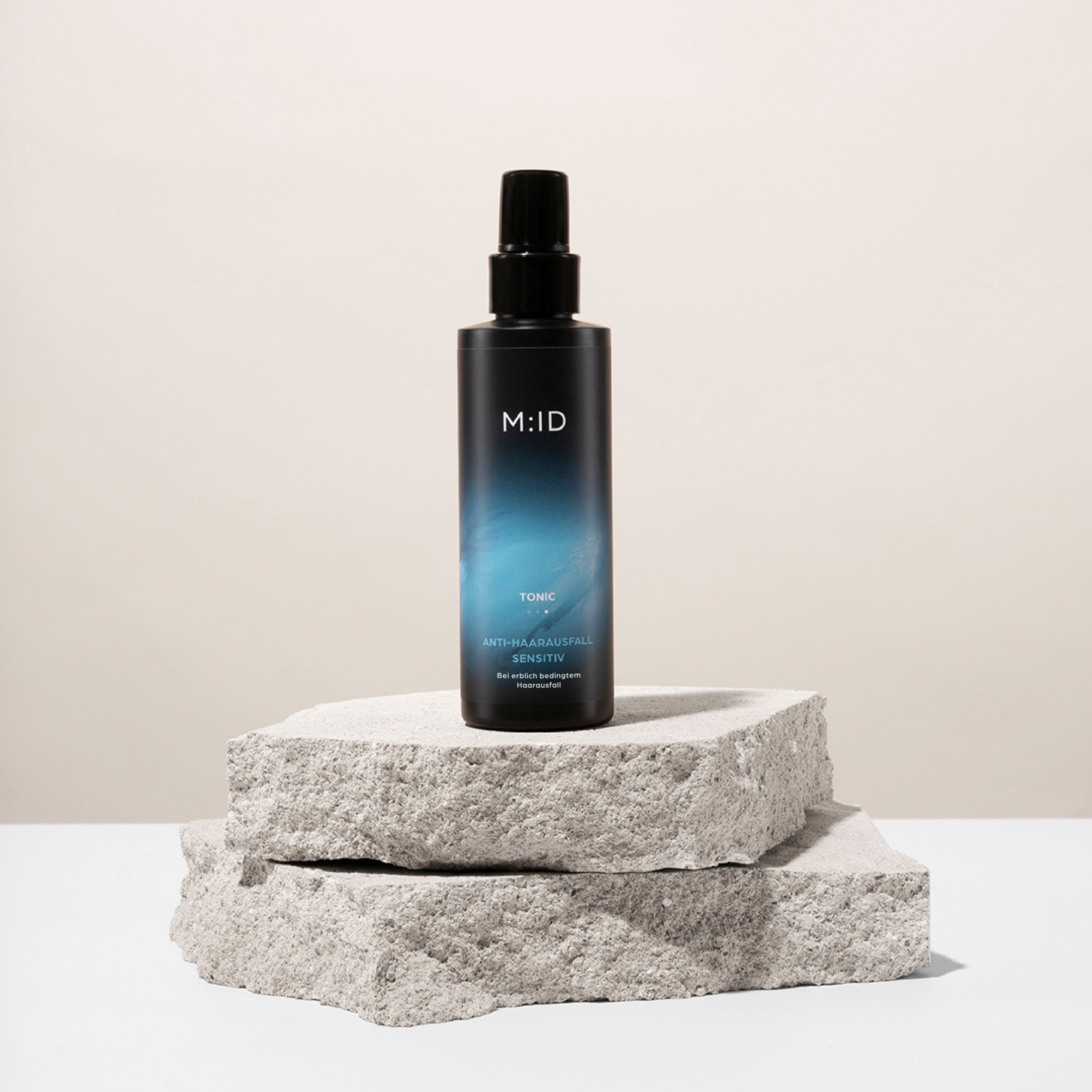 Schwarze Flasche auf Stein. Aufschrift: M:ID, Tonic, Anti-Haarausfall Sensitiv.