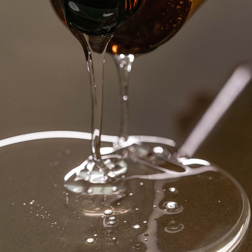 Klares Shampoo wird aus einer Flasche gegossen. Es bildet einen flüssigen Kreis auf einer Oberfläche.