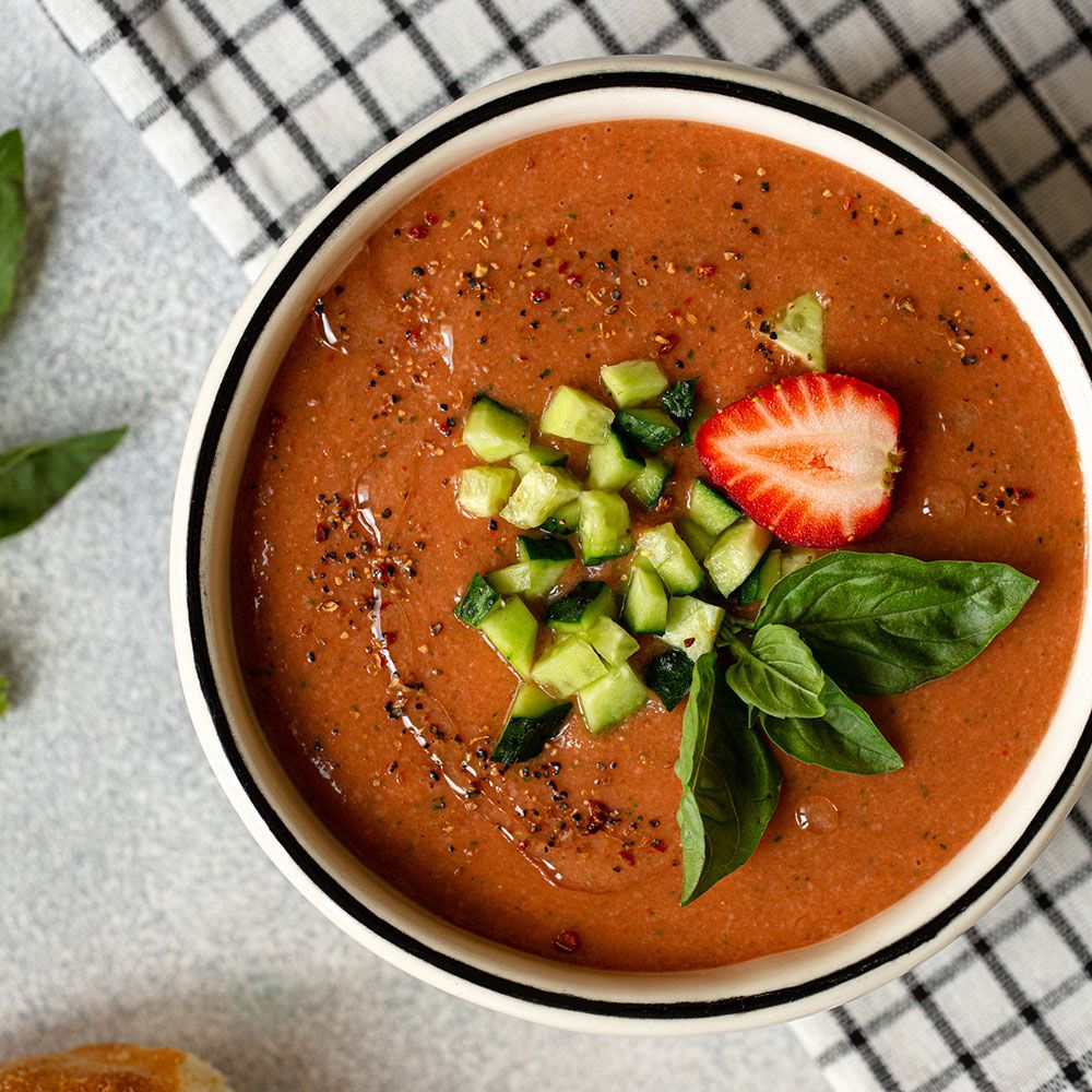 Rote Suppe in einer Schüssel. Gurkenwürfel, Erdbeerscheibe und Basilikumblätter als Garnitur.