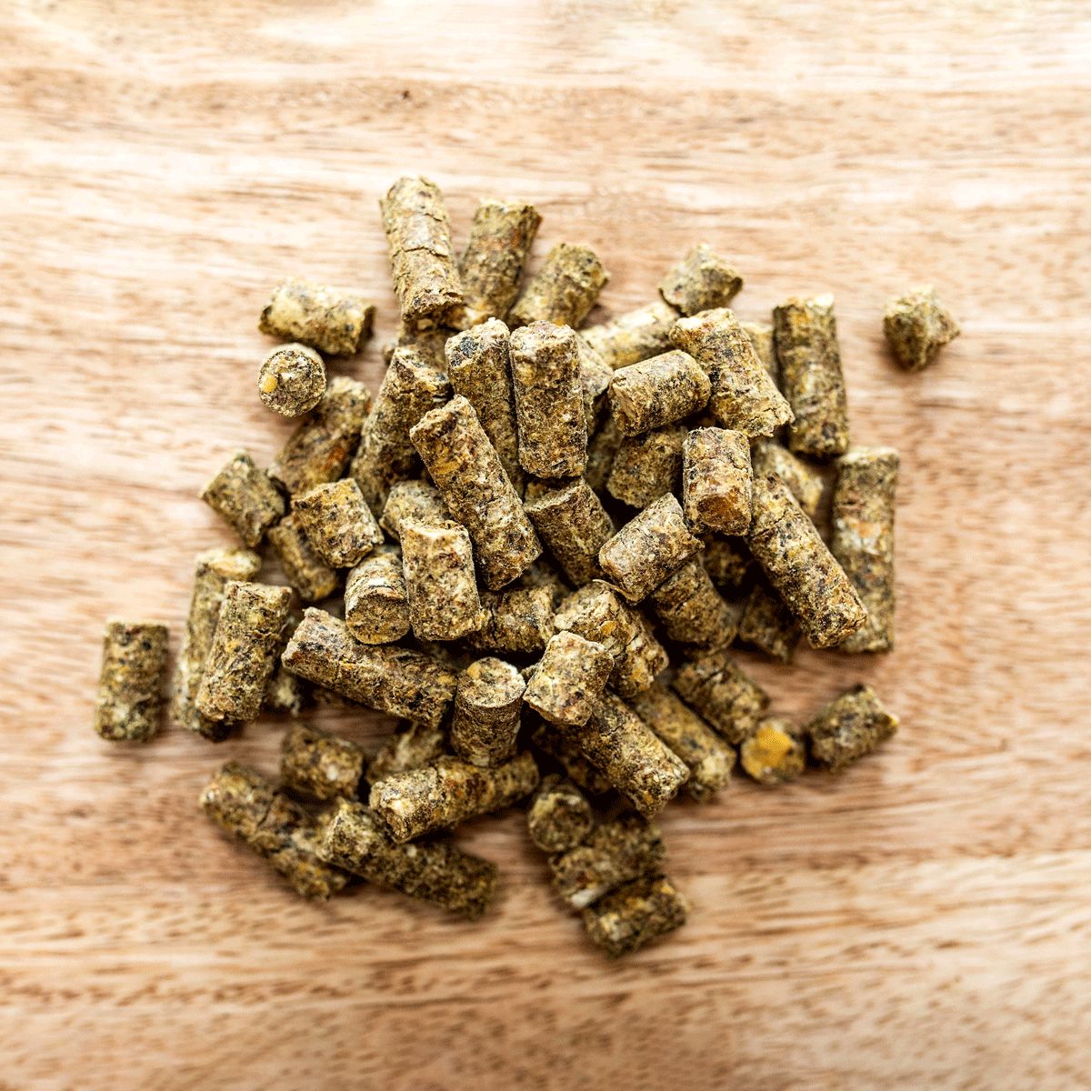 Haufen von zylindrischen Pellets auf Holzuntergrund. Grünlich-braune Farbe, unterschiedliche Größen.