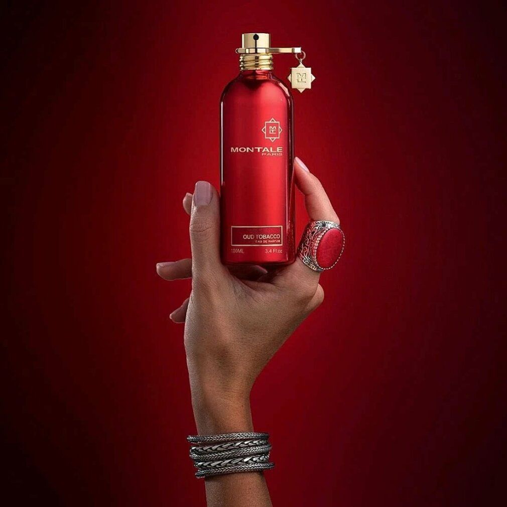 Rote Flasche mit goldfarbenem Verschluss und Anhänger, gehalten von einer Hand. Aufschrift: MONTALE PARIS, Oud Tobacco.