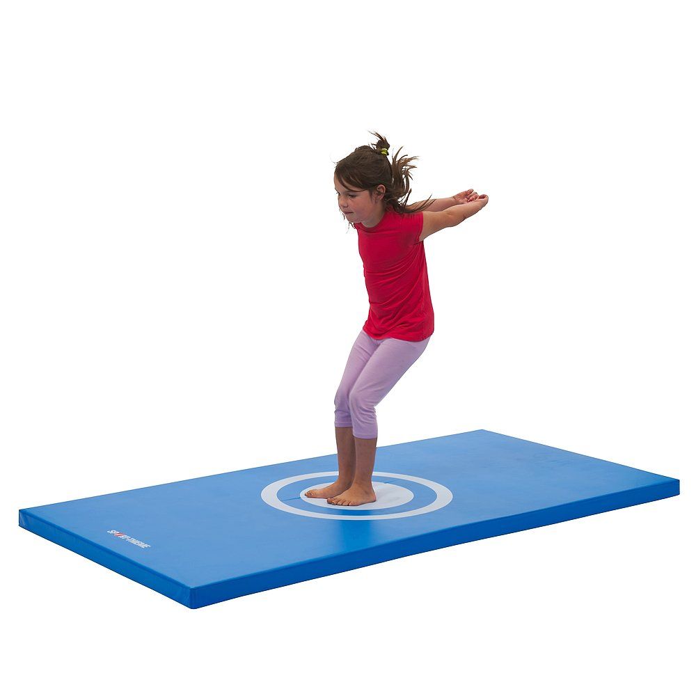 Blaue Turnmatte mit weißem Zielkreis. Ein Mädchen springt auf der Matte. Sie trägt ein rotes Oberteil und eine rosa Hose.