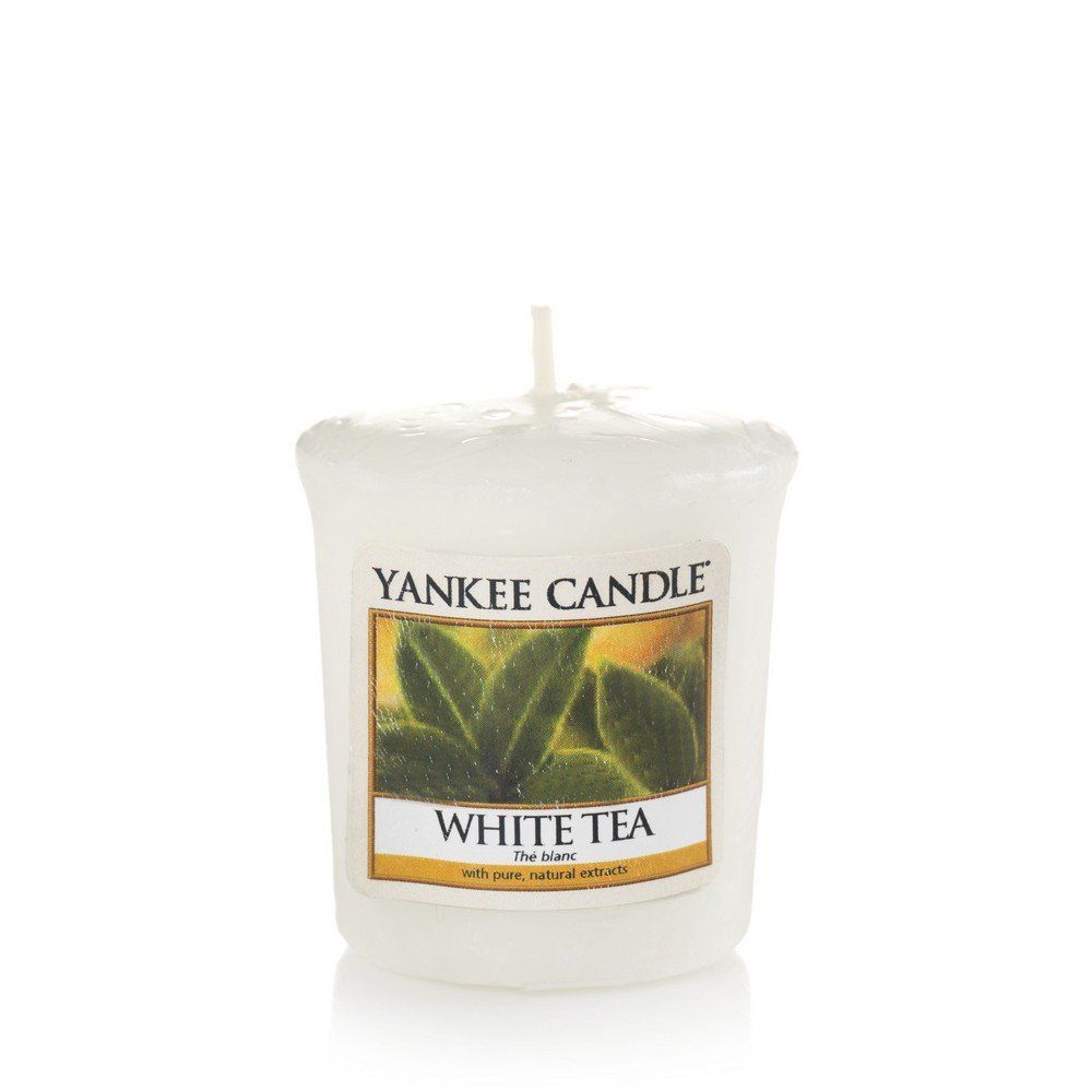 Weiße Kerze mit Aufschrift "Yankee Candle White Tea". Auf dem Etikett sind grüne Blätter abgebildet. Ein Docht ragt heraus.