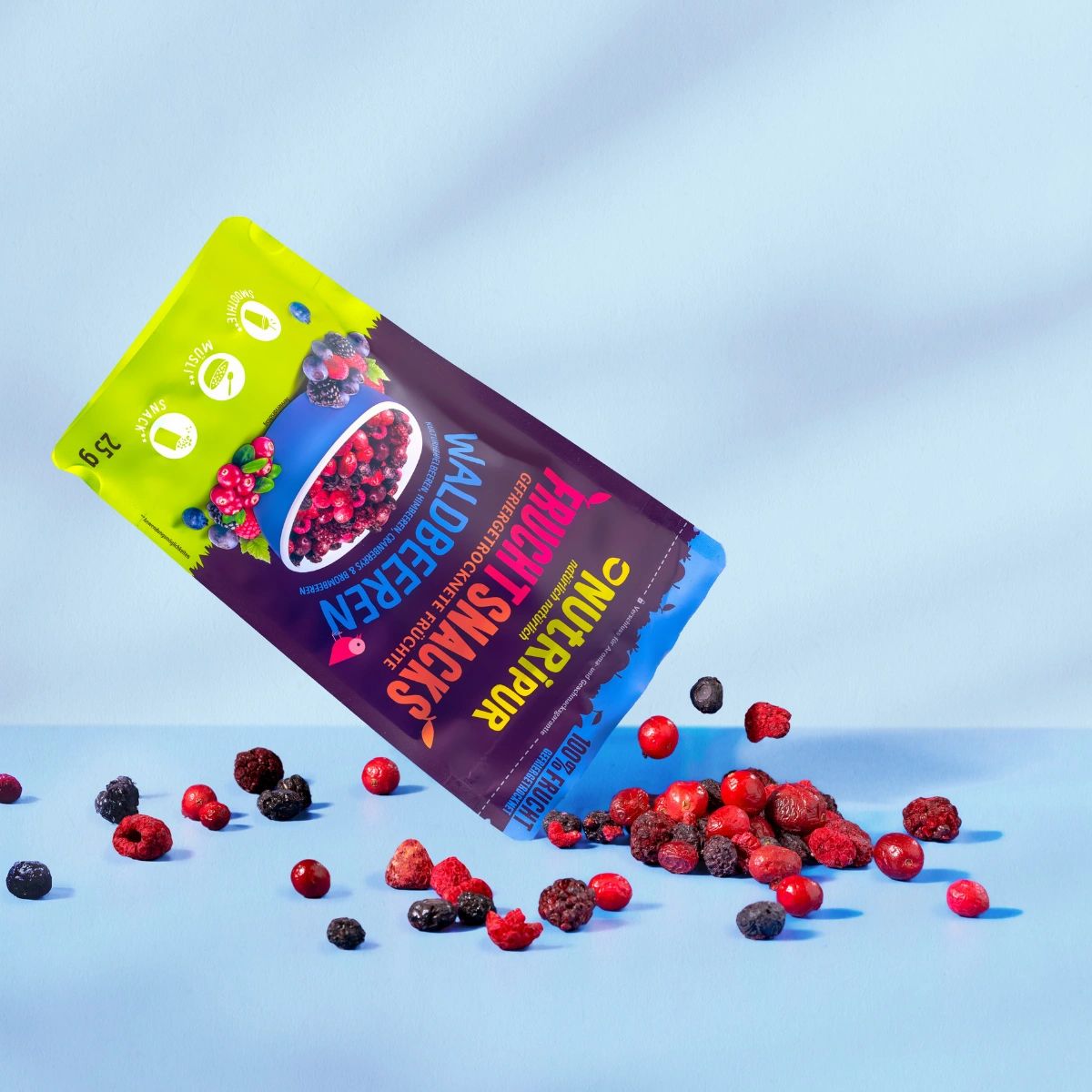 Beutel NutriPur Frucht-Snacks Waldbeeren, Inhalt fällt heraus. Auf blauem Hintergrund. Einige Beeren liegen verstreut.