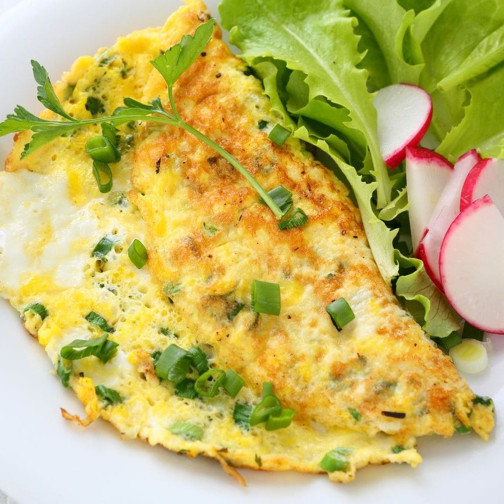 Omelett auf weißem Teller mit Salat und Radieschen. Gelbes Omelett mit grünen Kräutern.