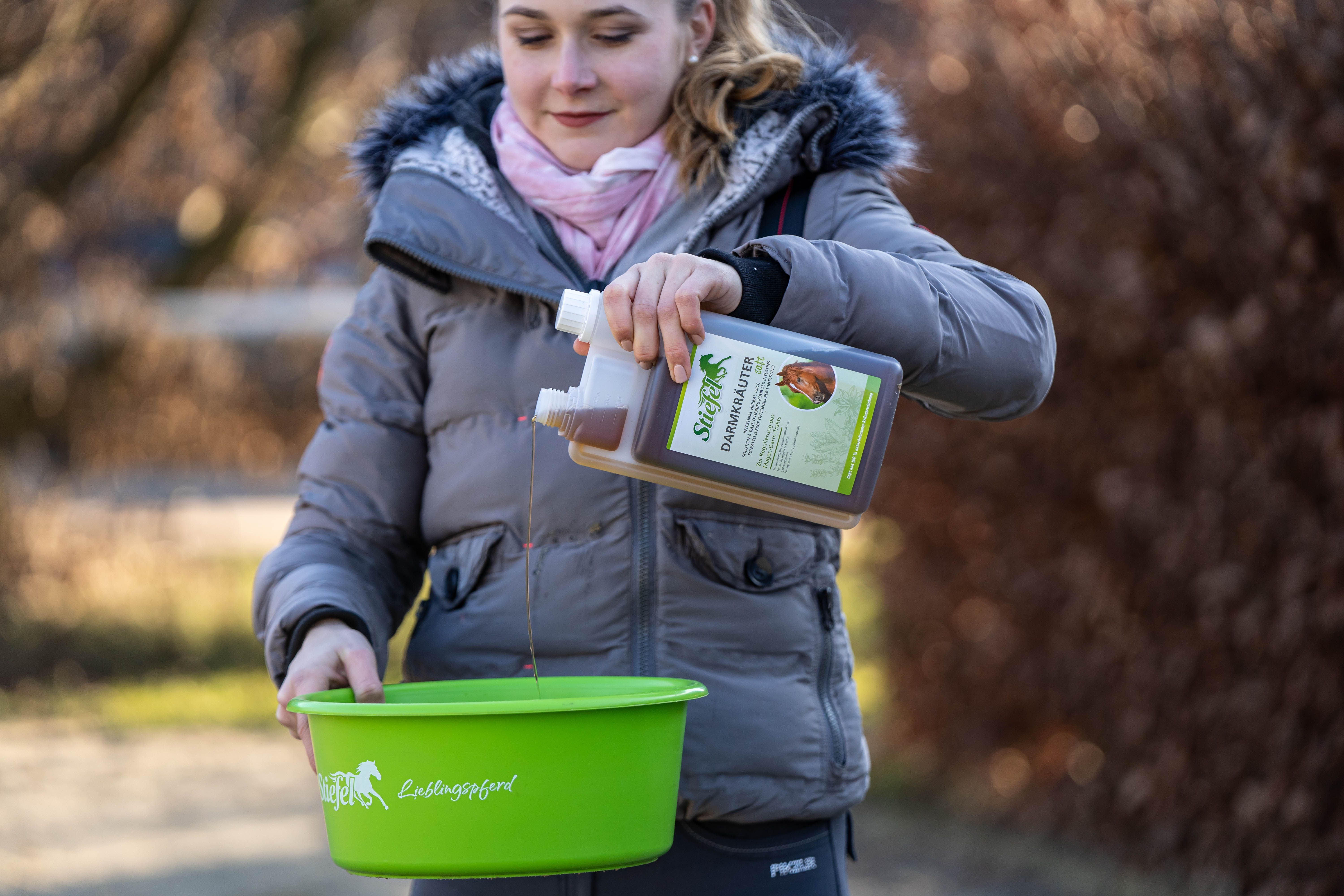 Person gießt braune Flüssigkeit aus einer Flasche Stiefel Darmkräutersaft in einen grünen Behälter.