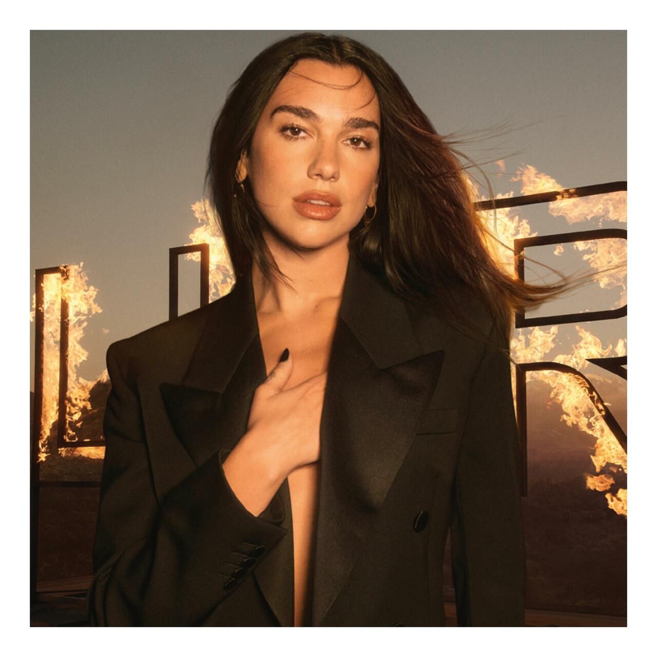 Eine Frau mit dunklen Haaren und schwarzem Blazer. Im Hintergrund ist ein Schriftzug zu sehen.