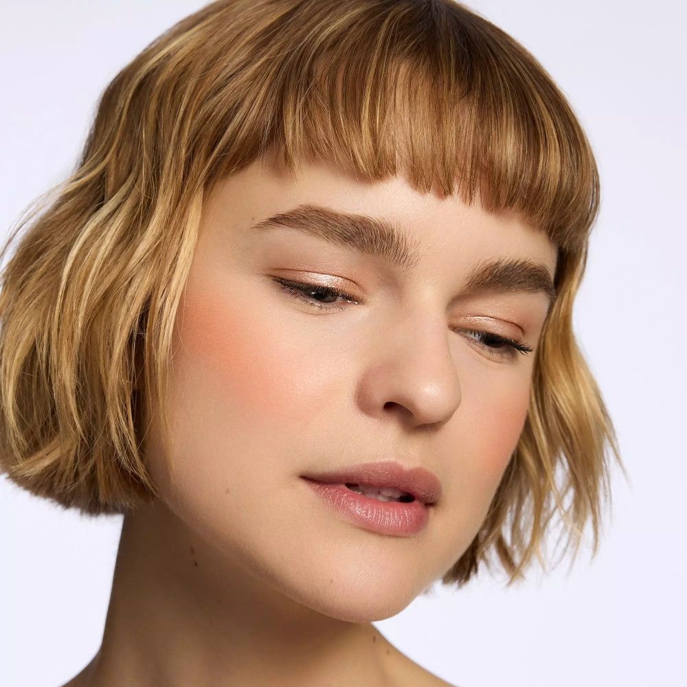 Porträt einer Frau mit Rouge auf den Wangen. Kurze blonde Haare. Blick nach unten.