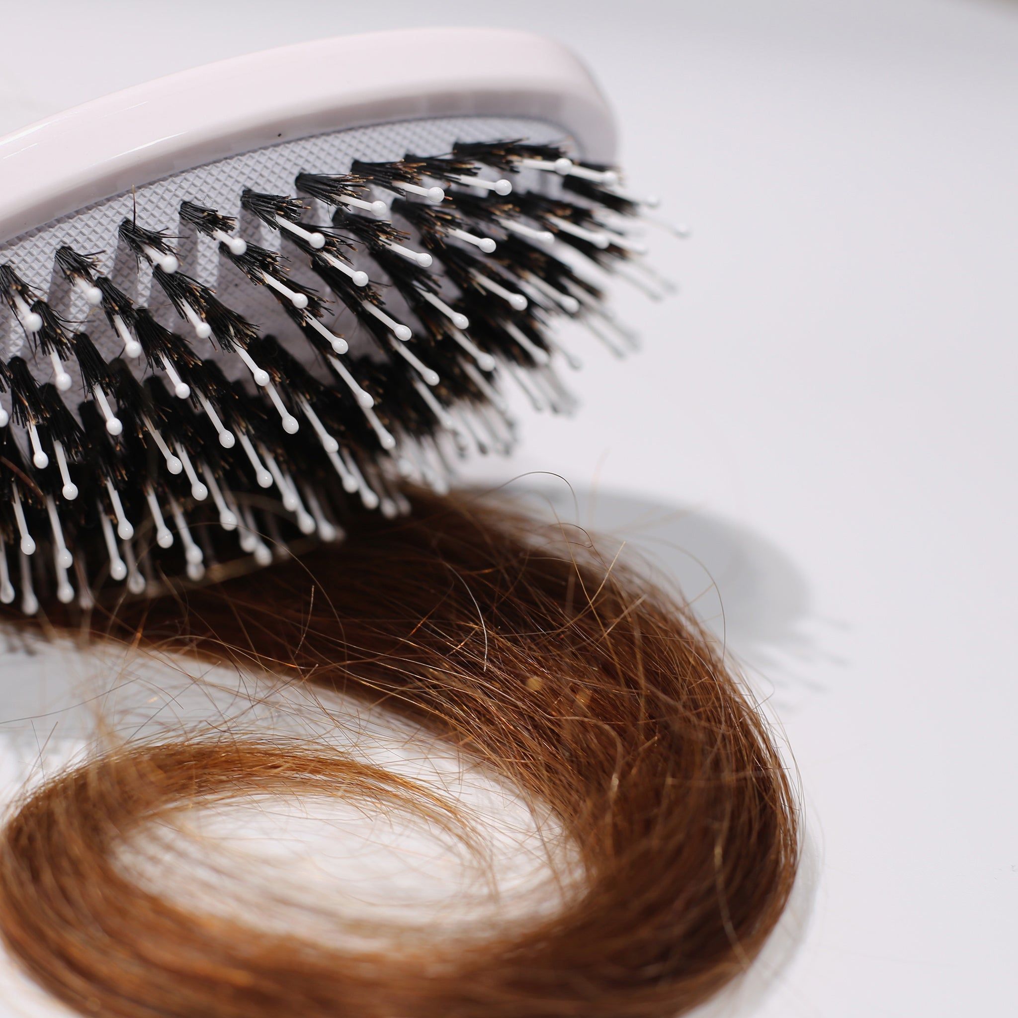 Nahaufnahme einer weißen Bürste mit schwarzen Borsten und einem Haarstrang.