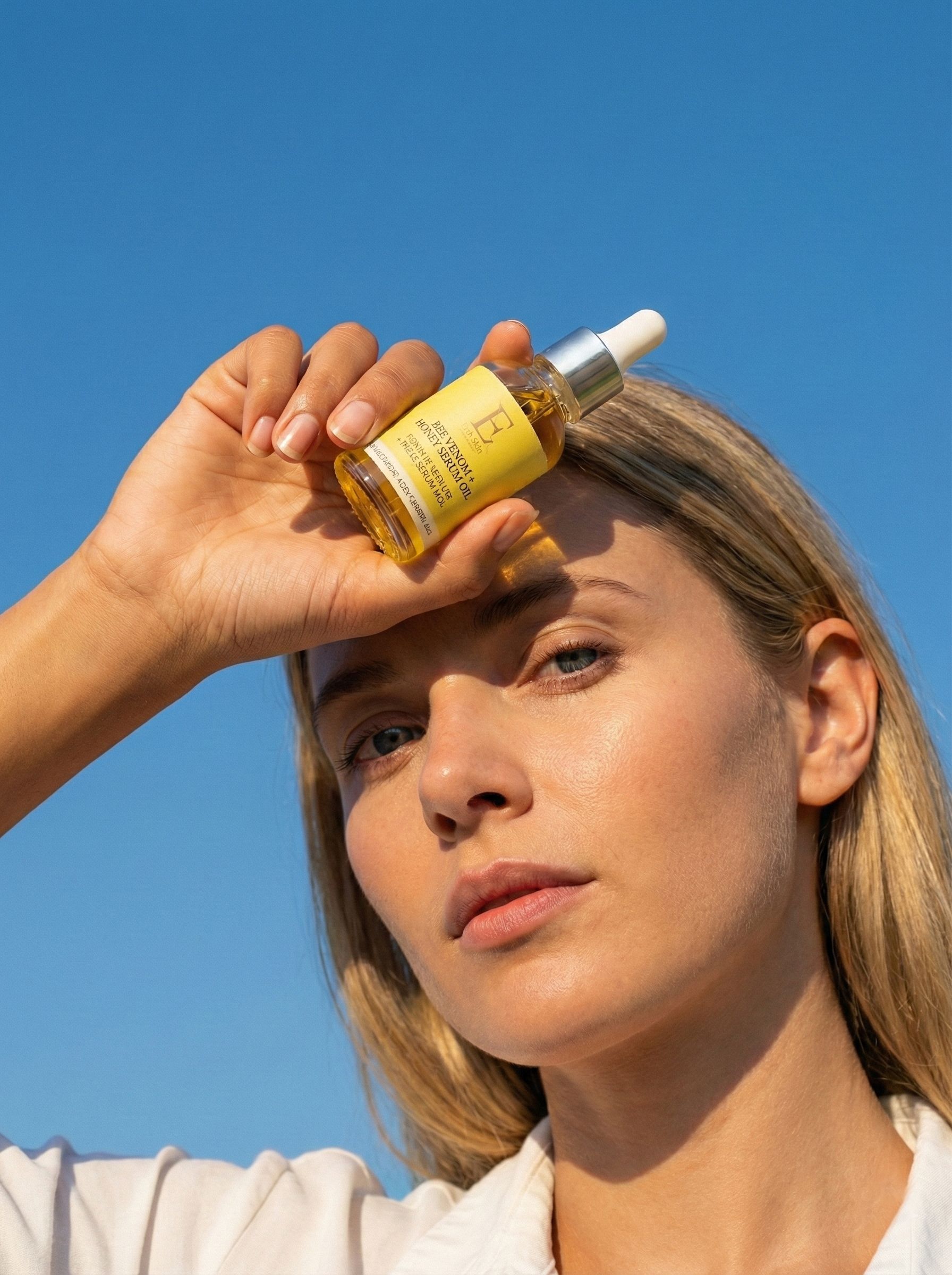 Frau hält eine kleine Glasflasche mit Serum vor dem Gesicht, blauer Himmel.