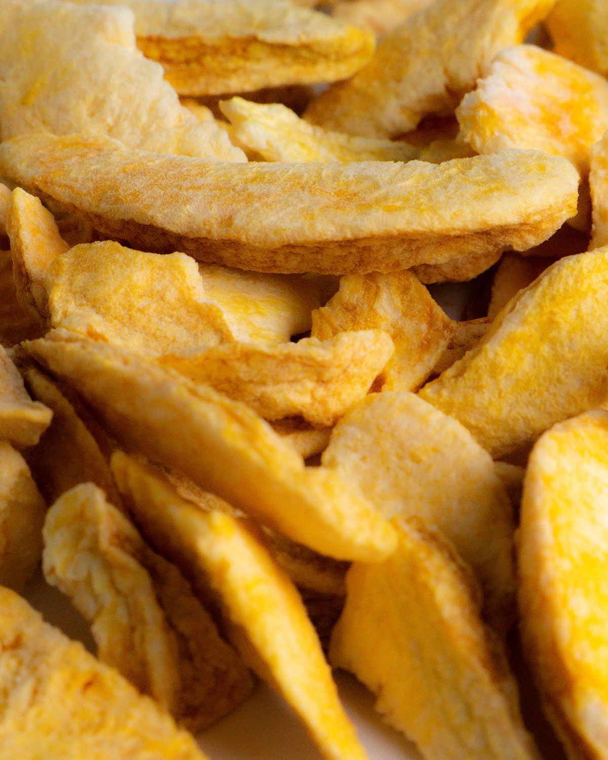 Nahaufnahme von getrockneten Pfirsichscheiben. Gelbliche Farbe. Viele Scheiben liegen dicht beieinander.