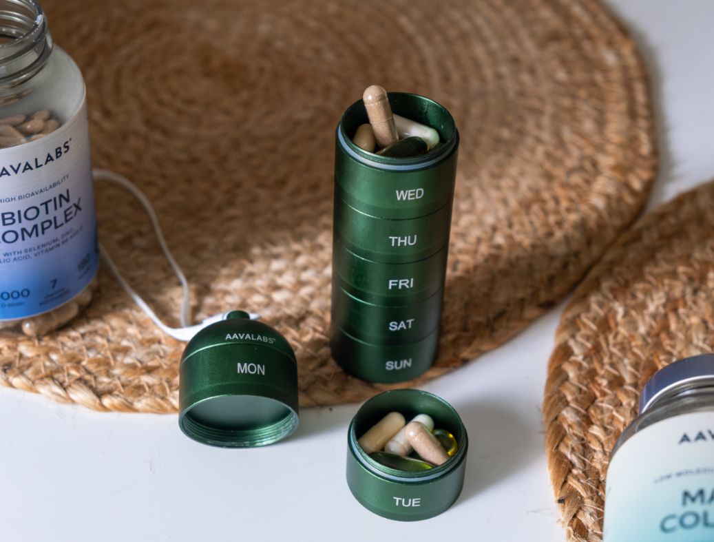 Grüne Pillendose mit 7 Fächern, daneben Pillenflaschen und offene Fächer mit Pillen.