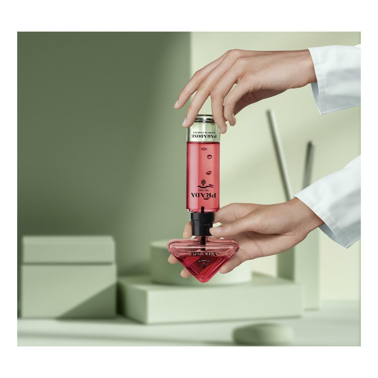 Hände halten Flakon und Nachfüllung. Roter Flakon, transparente Nachfüllung. Text: PARADOXE.