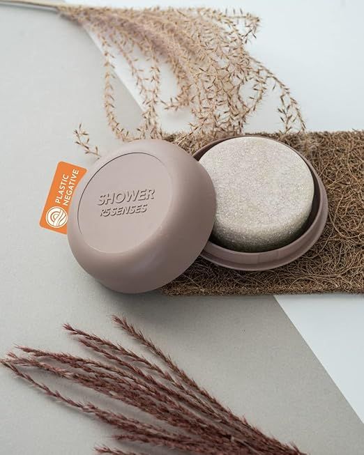 Geöffneter, brauner Behälter mit Seife. Deckel mit Schriftzug „SHOWER ESSENSES“. Orangefarbenes Etikett „PLASTIC NEGATIVE“.
