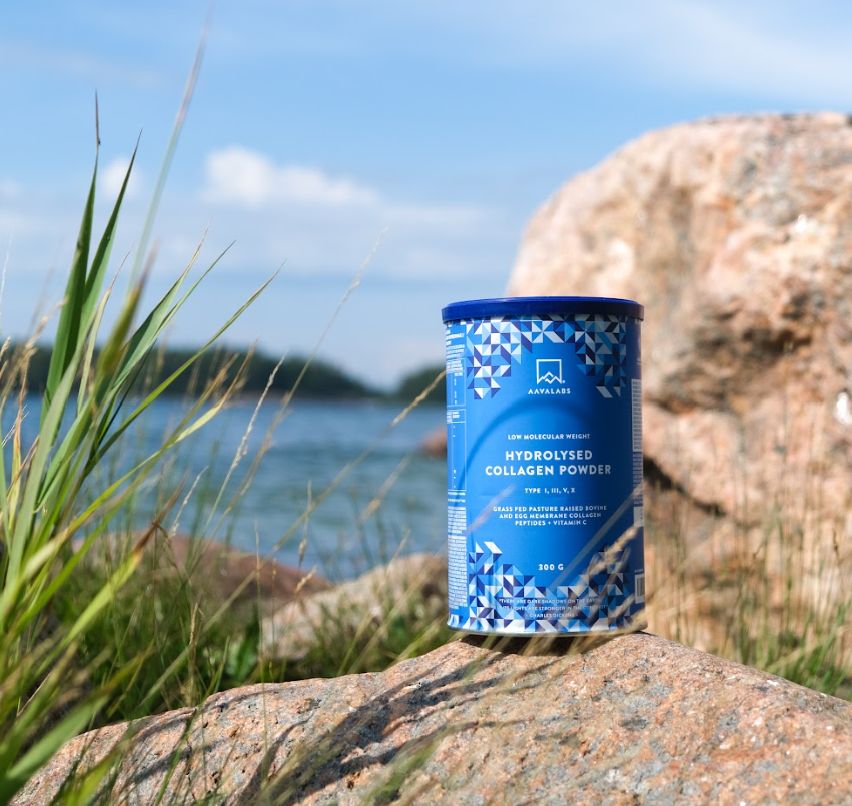 Blaue Dose Kollagenpulver auf einem Felsen, im Hintergrund Wasser und Himmel. Produktname sichtbar.