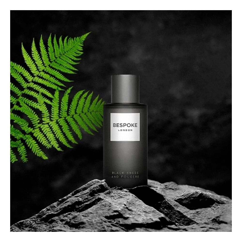 Dunkle Flasche auf Stein. "BESPOKE LONDON" auf weißem Etikett. Text: "BLACK SUEDE AND FOUGERE". Grünes Blatt im Hintergrund.
