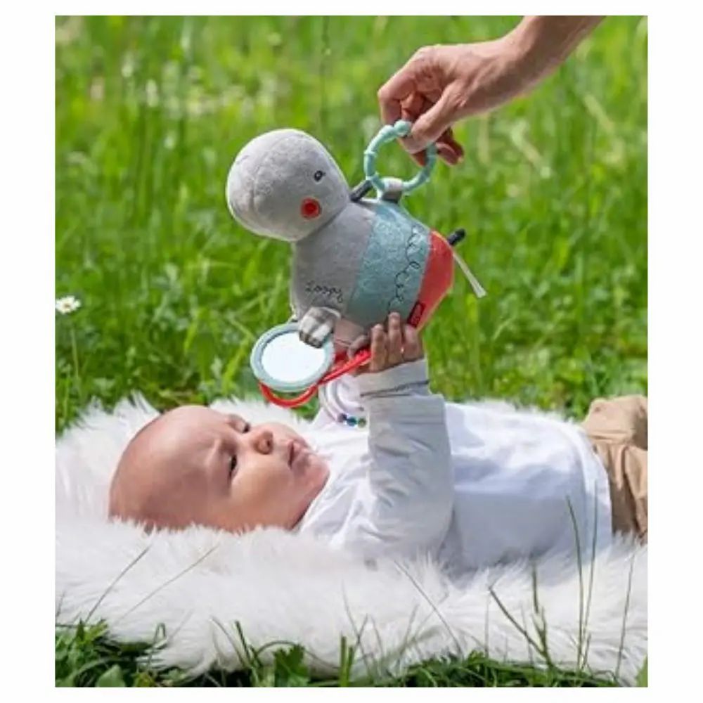 Baby liegt auf Decke, Hand hält Nilpferd-Kuscheltier. Spielzeug mit Spiegel und Ringen. Baby schaut.