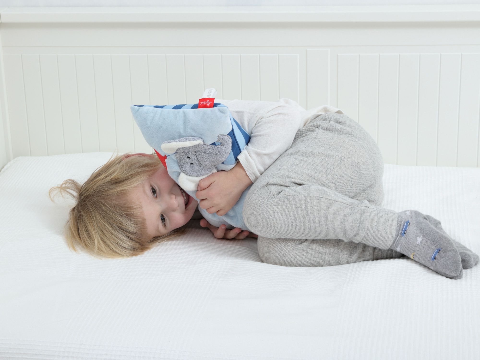 Kleinkind umarmt blaues Kissen mit Elefanten-Applikation. sigikid-Label sichtbar.