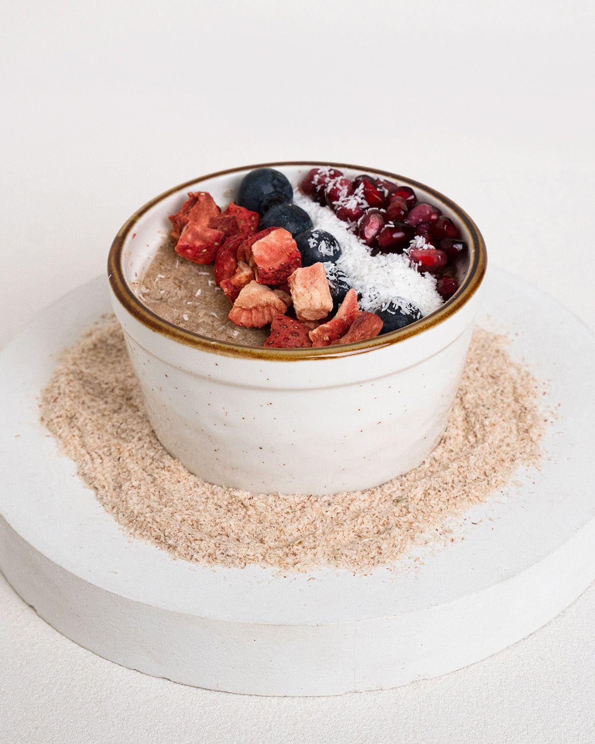 Schale mit Müsli und Früchten. Auf weißem Untergrund, umgeben von Flohsamenschalen.