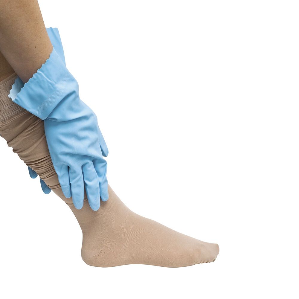 Person trägt Kompressionsstrumpf. Blaue Handschuhe helfen beim Anziehen. Hautfarbener Strumpf bedeckt Bein und Fuß.