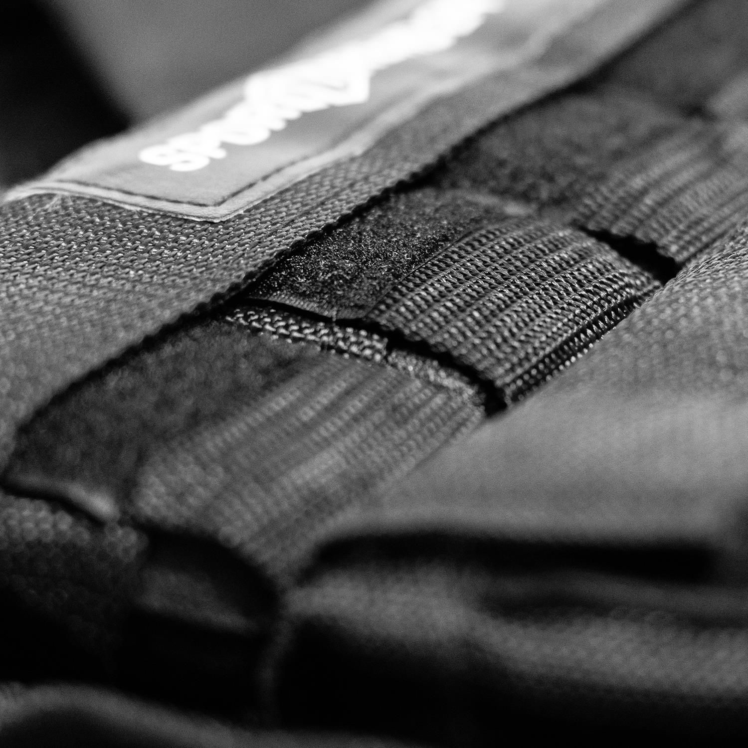 Nahaufnahme des Logos Sporttrend24 auf der schwarzen Gewichtsweste. Klettverschluss.