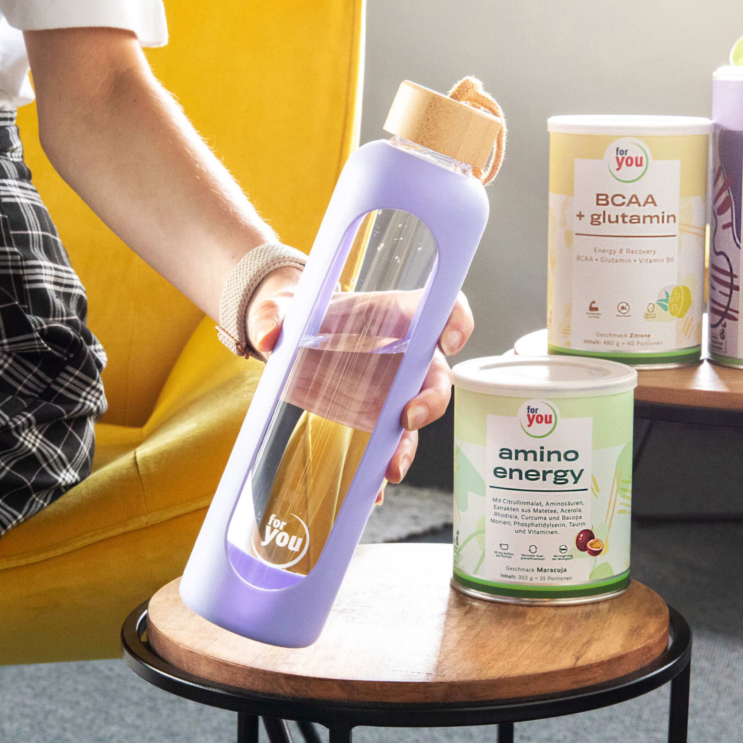 Lila Glasflasche mit Holzdeckel, daneben Dosen mit 'Amino Energy' und 'BCAA + Glutamin'.