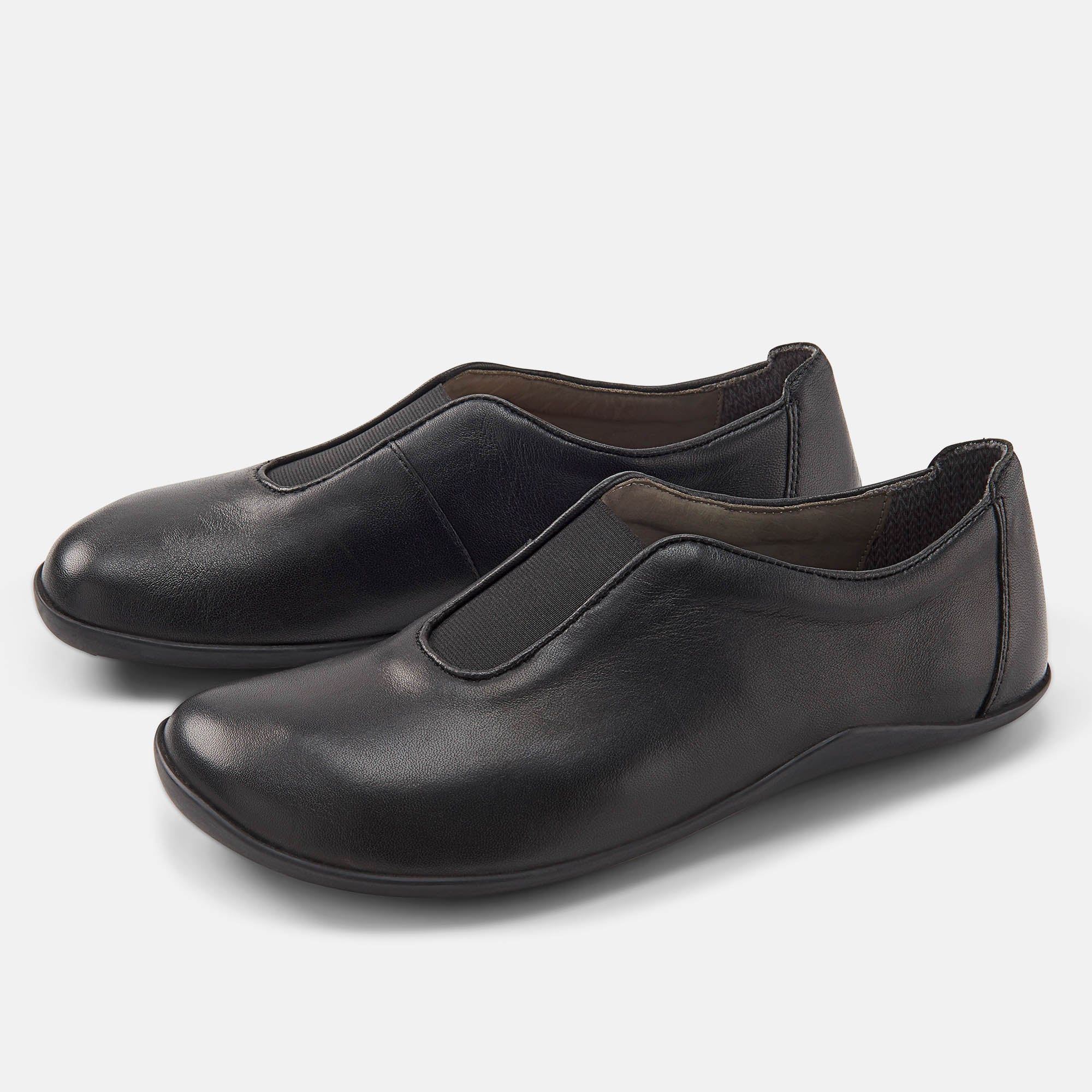 Zwei schwarze Slipper. Obermaterial Leder, breite Passform. Elastischer Einsatz am Spann. Flache Sohle.