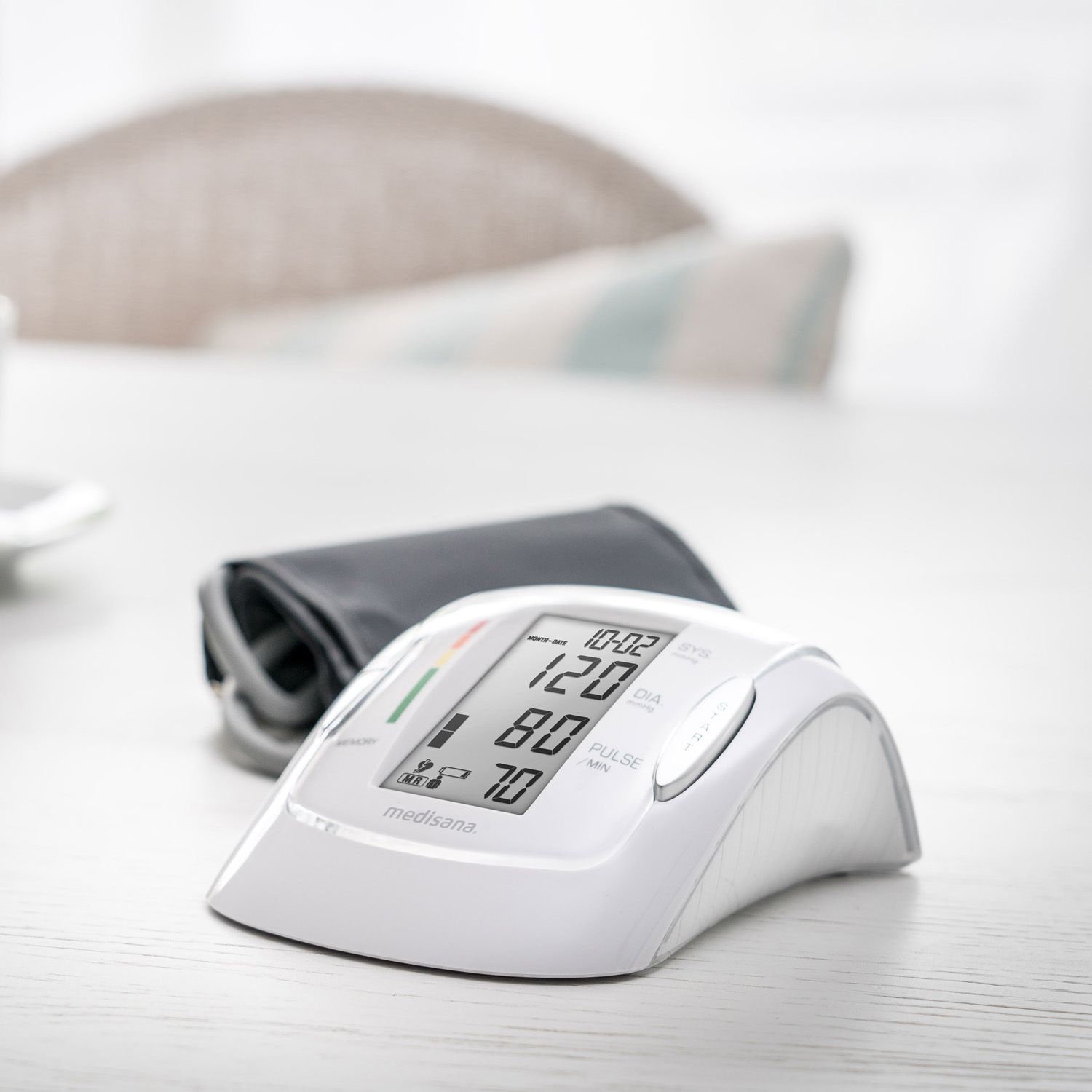 Bloeddrukmeter met digitale display. Toont waarden. Witte behuizing, grijze manchet ernaast. Merk: medisana.