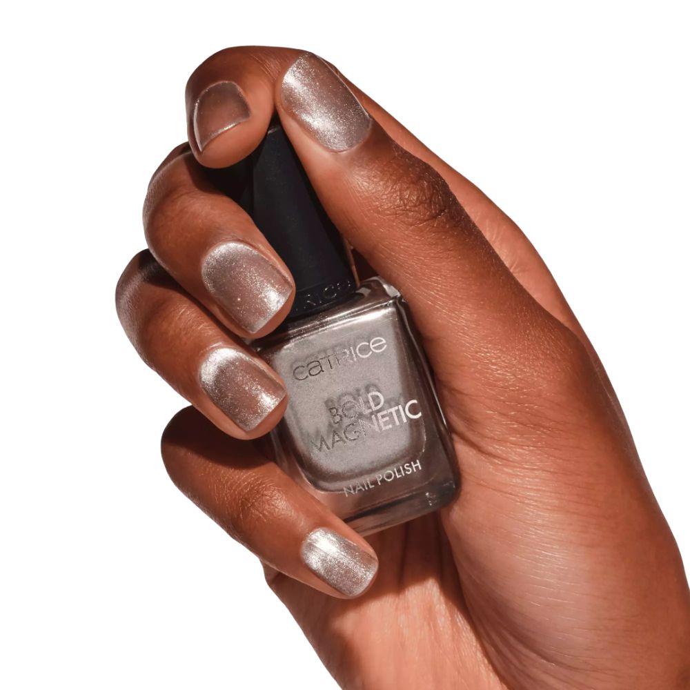 Hand mit lackierten Nägeln und Nagellackflasche. Aufschrift: Catrice, Bold Magnetic, Nail Polish. Farbtöne: Silber, Grau.