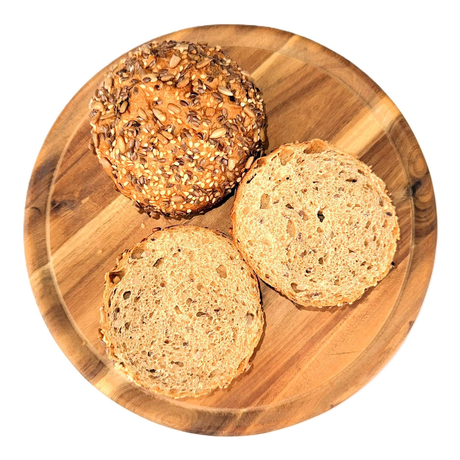 Drei Brötchenhälften auf einem Holzbrett. Ein Brötchen ist ganz, die anderen beiden sind halbiert. Sichtbar sind Körner und Samen.