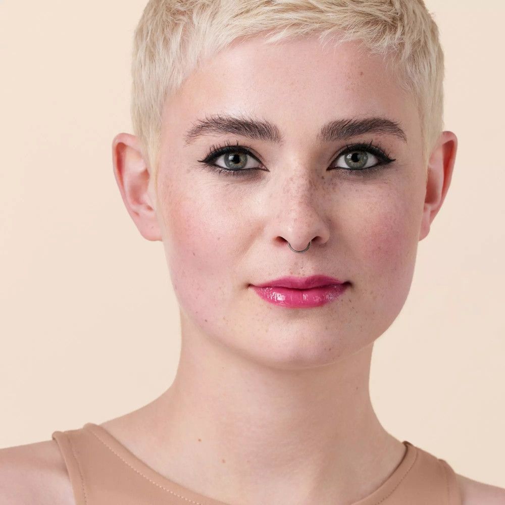 Porträt einer Frau mit blonden, kurzen Haaren. Sie trägt Make-up, einschließlich glänzender Lippen.